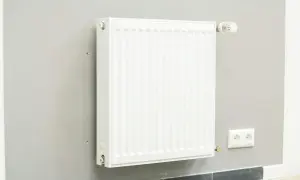 Biały grzejnik z termostatem na szarej ścianie. Dowiedz się, jak wymienić grzejnik w sezonie grzewczym, aby zapewnić ciepło w domu.