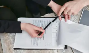 Dwie osoby analizują dokument, który może być umową deweloperską. Wskazują na tekst i wypełniają formularz.