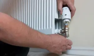 Ręce montują nowy termostat do grzejnika. Wymiana termostatu w grzejniku to prosty sposób na oszczędność energii.