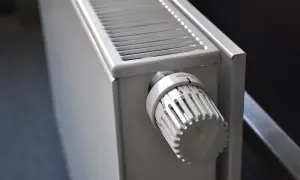 Biały grzejnik z termostatem. Pokrętło pokazuje ustawienie 3. Dowiedz się, jak spuścić wodę z grzejnika, aby przygotować go do sezonu.