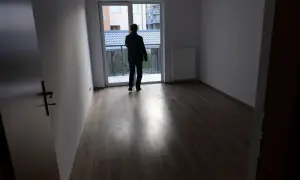 Mężczyzna w pustym mieszkaniu, zastanawia się, gdzie złożyć wniosek o mieszkanie komunalne. Widok na balkon i sąsiednie budynki.