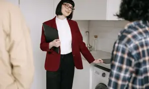 Kobieta z teczką wyjaśnia, co jest potrzebne do wymeldowania się z mieszkania. Rozmowa z klientami w kuchni.