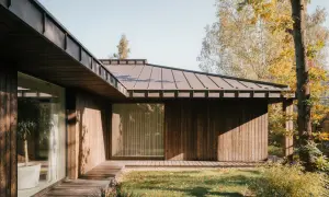 Nowoczesna stodoła z drewnianą elewacją i metalowym dachem, otoczona jesienną zielenią.
