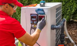 Technik w czerwonej koszulce i czapce podłącza pompę ciepła monoblok. Widać narzędzia i elementy instalacji.