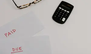 Okulary, kalkulator i dokumenty z napisami "PAID" i "DUE" sugerują rozliczenia, być może związane z nowym podatkiem od nieruchomości.