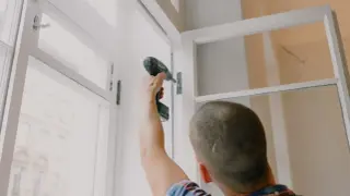 Mężczyzna przykręca zawias okna. Zastanawiasz się, ile kosztuje wymiana okien w bloku?