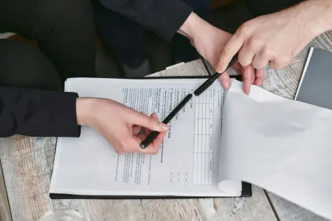 Dwie osoby analizują dokument, który może być umową deweloperską. Wskazują na tekst i wypełniają formularz.