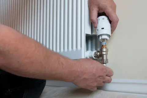 Ręce montują nowy termostat do grzejnika. Wymiana termostatu w grzejniku to prosty sposób na oszczędność energii.
