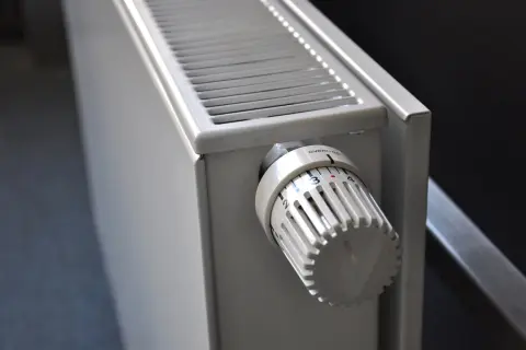 Biały grzejnik z termostatem. Pokrętło pokazuje ustawienie 3. Dowiedz się, jak spuścić wodę z grzejnika, aby przygotować go do sezonu.