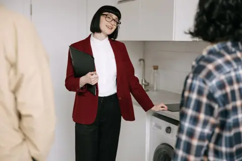 Kobieta z teczką wyjaśnia, co jest potrzebne do wymeldowania się z mieszkania. Rozmowa z klientami w kuchni.