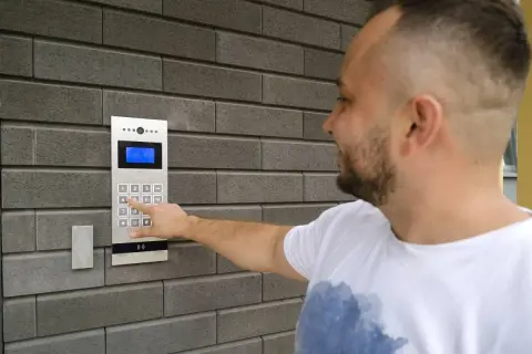 Mężczyzna naciska cyfrę na domofonie, pokazując, jak działa domofon w bloku.