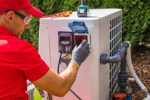 Technik w czerwonej koszulce i czapce podłącza pompę ciepła monoblok. Widać narzędzia i elementy instalacji.