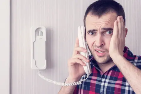 Zmartwiony mężczyzna dzwoni z telefonu domofonowego. Gdzie zgłosić niedziałający domofon?