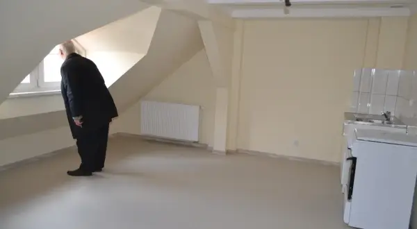 Mężczyzna w garniturze ogląda nowe mieszkanie, zastanawiając się, jak złożyć wniosek o mieszkanie z miasta. Widać kuchnię i okno.