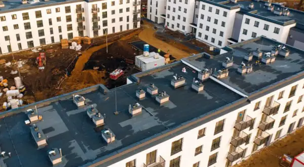 Budowa osiedla mieszkanie plus w trakcie. Nowe bloki z balkonami, plac budowy z koparką i materiałami.