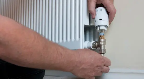 Ręce montują nowy termostat do grzejnika. Wymiana termostatu w grzejniku to prosty sposób na oszczędność energii.