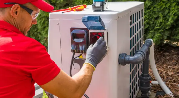 Technik w czerwonej koszulce i czapce podłącza pompę ciepła monoblok. Widać narzędzia i elementy instalacji.
