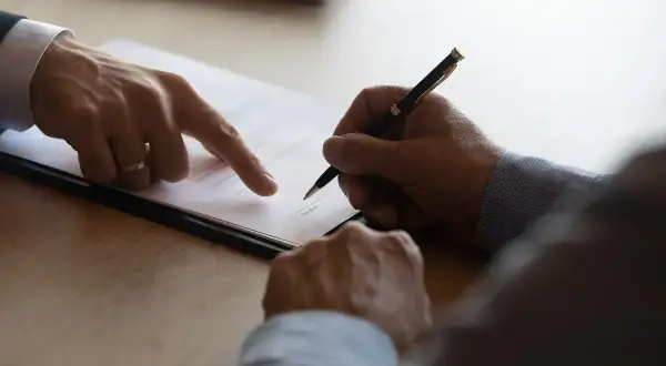 Podpisanie umowy, gdzie jeden mężczyzna wskazuje palcem na dokument, a drugi składa podpis. To ważny krok, by zabezpieczyć zadatek na mieszkanie.