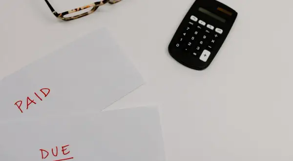 Okulary, kalkulator i dokumenty z napisami "PAID" i "DUE" sugerują rozliczenia, być może związane z nowym podatkiem od nieruchomości.