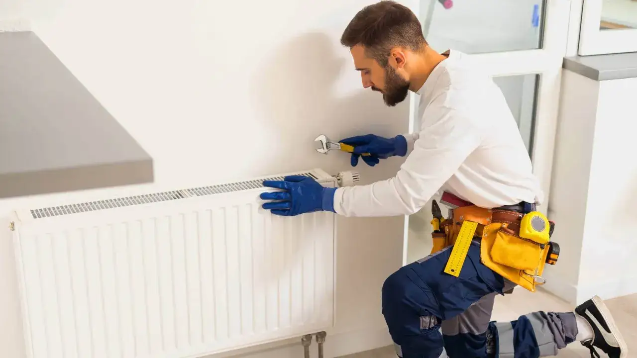 Instalator w niebieskich rękawiczkach używa klucza do grzejnika aluminiowego, pokazując, jak zrobić klucz do grzejników aluminiowych.