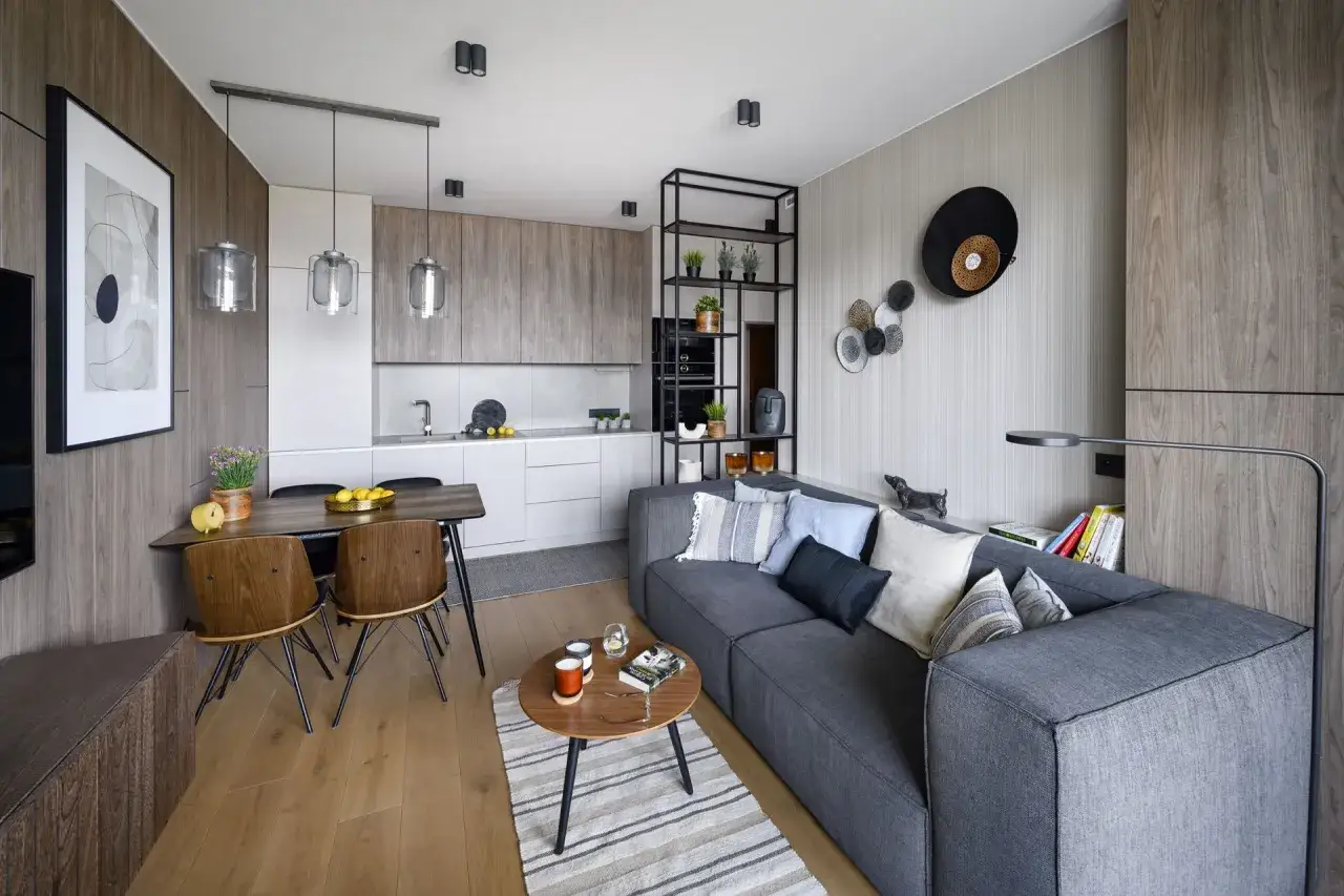 Nowoczesny salon w bloku: szara sofa, drewniane meble, kuchnia otwarta na salon. Inspiracja dla małych przestrzeni.