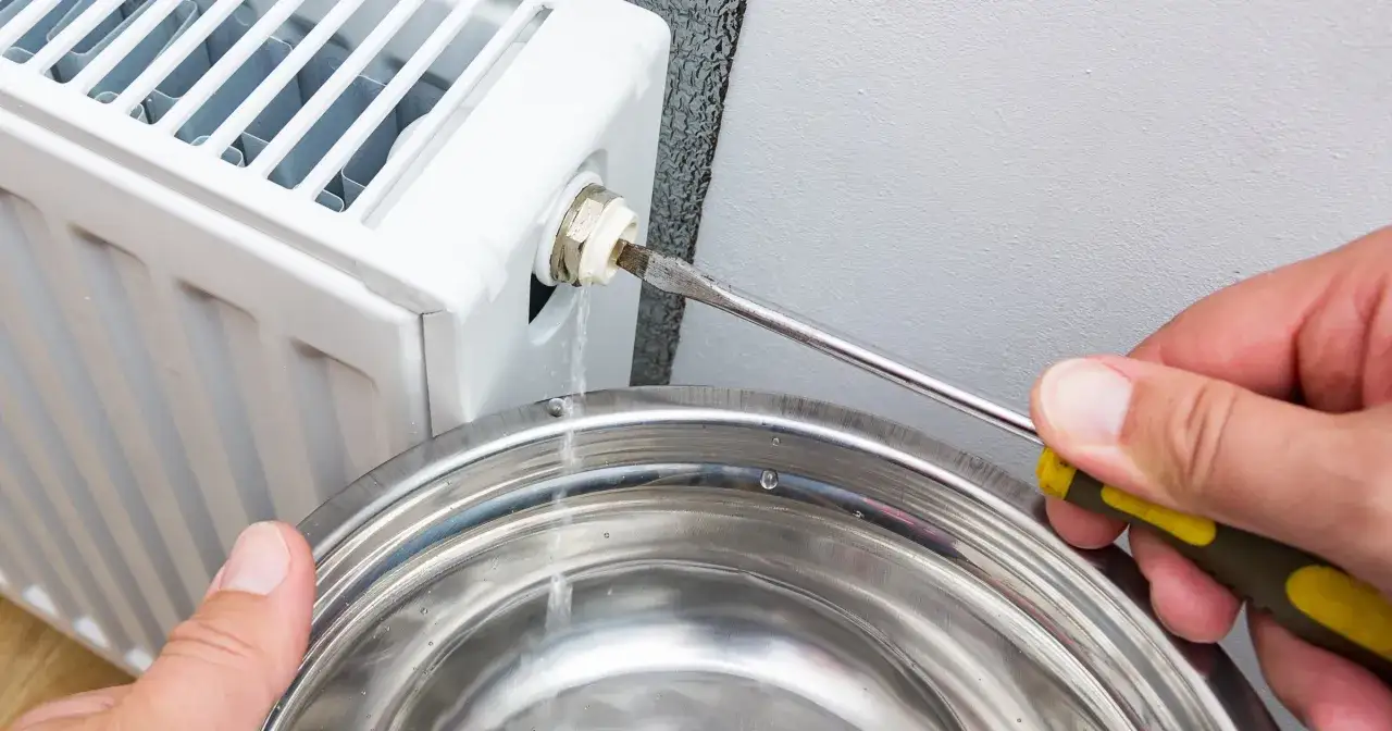 Odkręcanie odpowietrznika grzejnika aluminiowego. Woda kapie do miski.