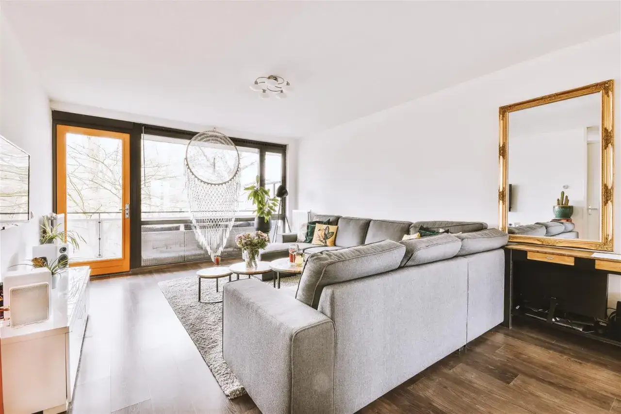 Nowoczesny salon w bloku: szara sofa, makrama, złote lustro i duży balkon. Inspiracja dla Ciebie!