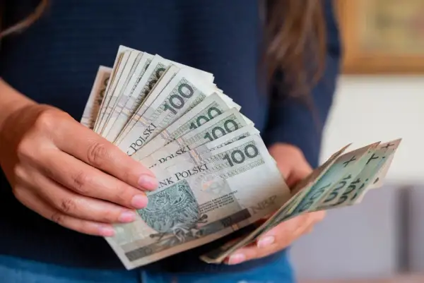 Dłonie trzymające stos banknotów 100 zł. Czy to przedpłata, czy zaliczka? Decyzja o płatności.