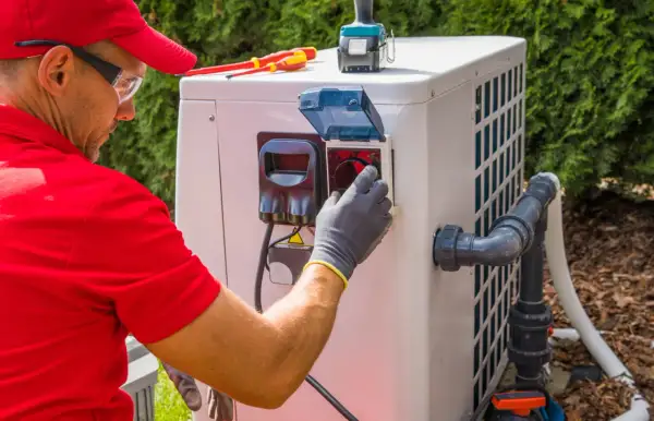 Technik w czerwonej koszulce i czapce podłącza pompę ciepła monoblok. Widać narzędzia i elementy instalacji.