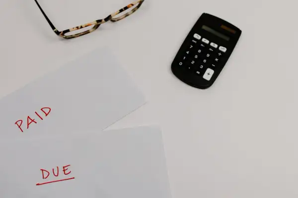 Okulary, kalkulator i dokumenty z napisami "PAID" i "DUE" sugerują rozliczenia, być może związane z nowym podatkiem od nieruchomości.